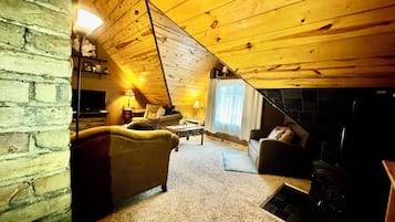 A cozy attic room with a fireplace, a sofa, and a television.
