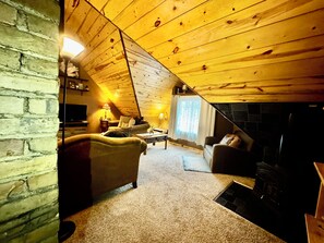 A cozy attic room with a fireplace, a sofa, and a television.