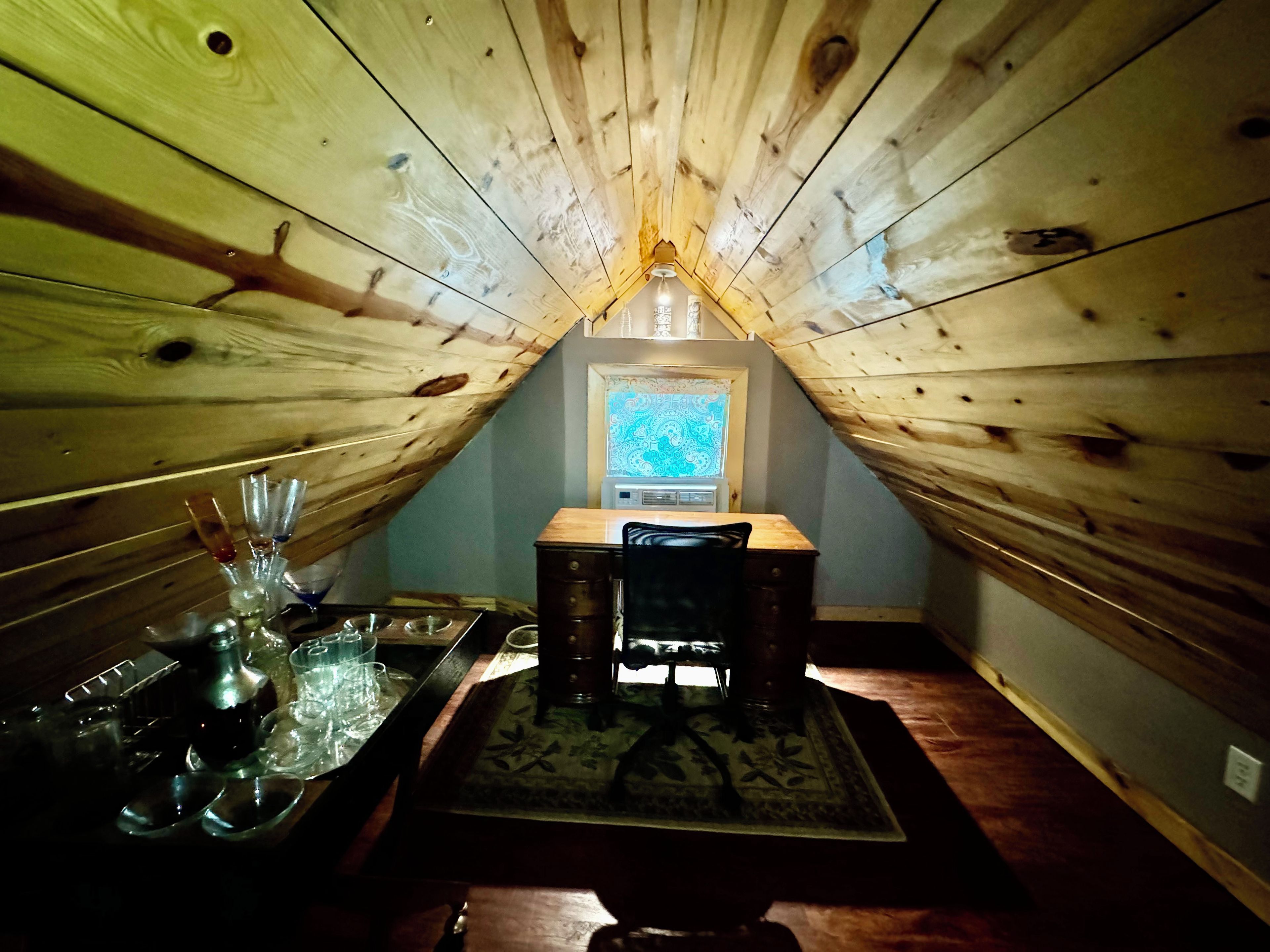 A cozy attic room with a sloped ceiling, a small window, a wooden table with a tray, and a chair.