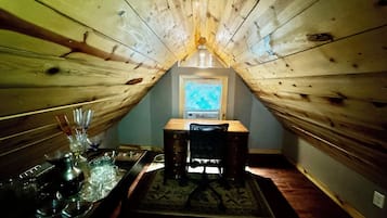 A cozy attic room with a sloped ceiling, a small window, a wooden table with a tray, and a chair.