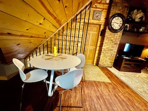 A dining area with a round table and chairs, a wooden staircase, a brick wall, and a television on a wooden stand. - Private Jacuzzi Penthouse in Charming 1890’s mansion (Saint Paul)