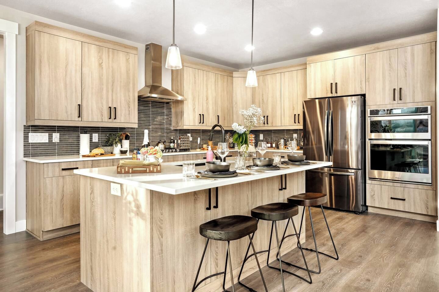 A modern kitchen with wooden cabinets, stainless steel appliances, and a central island with stools.