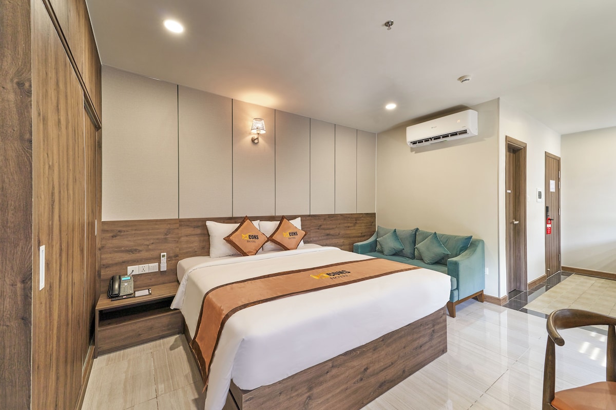 A hotel room with a large bed, a bedside table with a phone, a wall-mounted air conditioner, and a sofa.