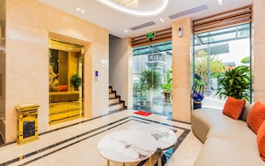 A hotel lobby with a marble floor, a reception desk, a sofa with orange cushions, and a glass entrance. - Bcons PS hotel (Tam Hiep)