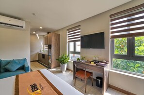 Een moderne hotelkamer met een bed, een bureau, een stoel, een televisie, een raam met zonwering en een kitchenette.