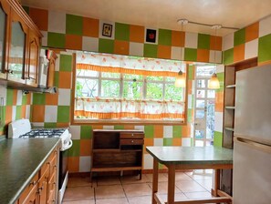 A kitchen with a gas stove, wooden cabinets, a window with a patterned curtain, and a tiled floor. - New Listing (Ciudad Nezahualcóyotl)