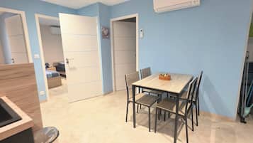 A compact kitchen with a dining table and chairs, a visible refrigerator, and a door leading to another room.