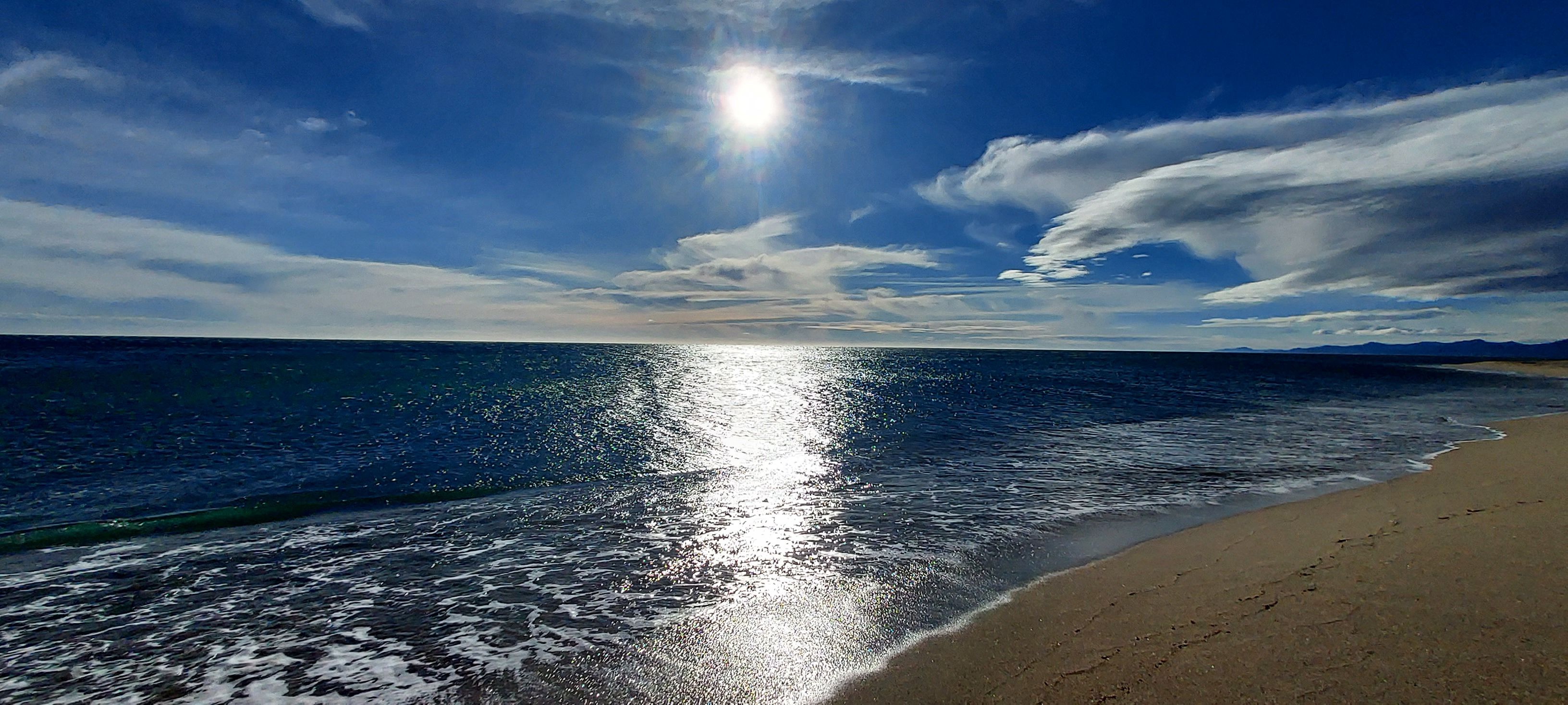 A beach with a clear sky and sunlight reflecting on the water.