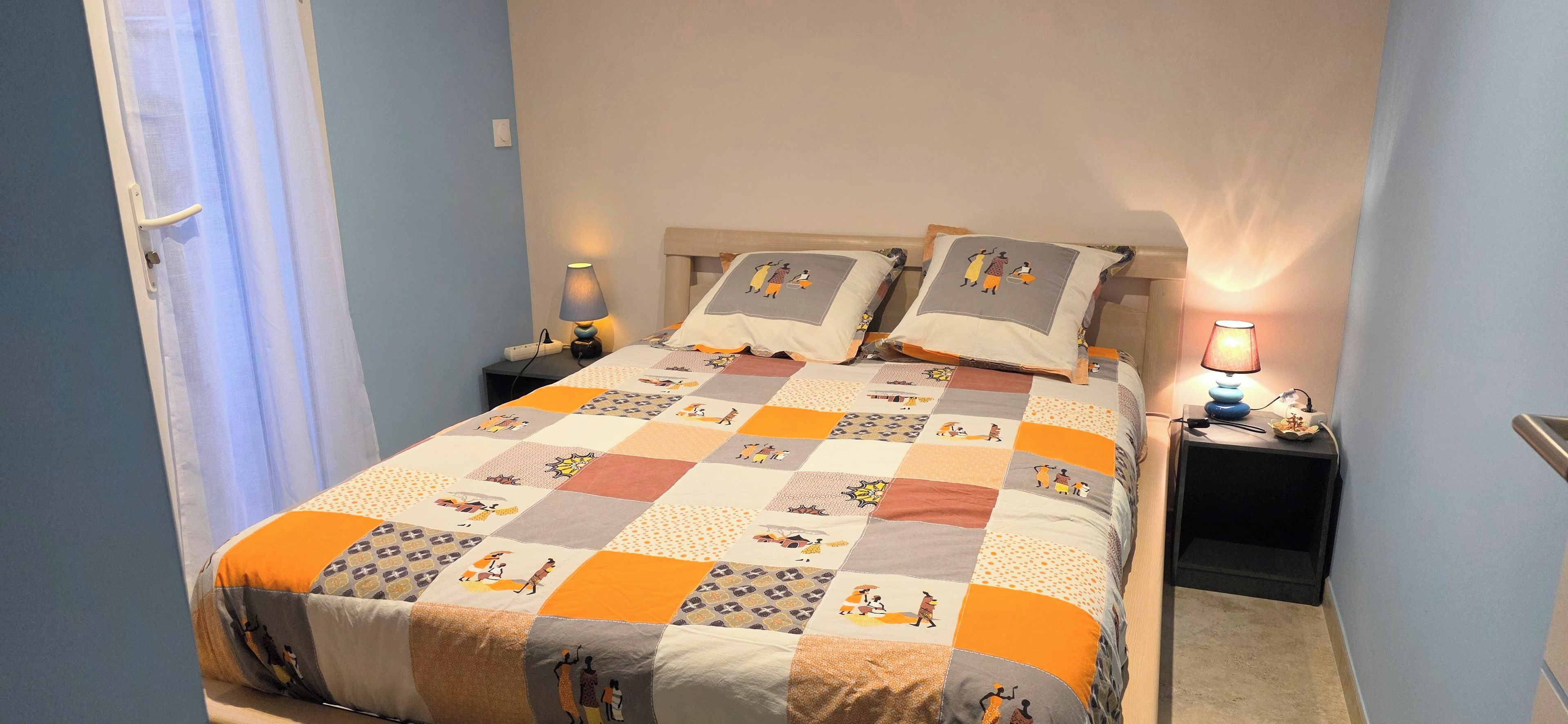 A bed with a quilt, two bedside lamps, and a window with curtains.