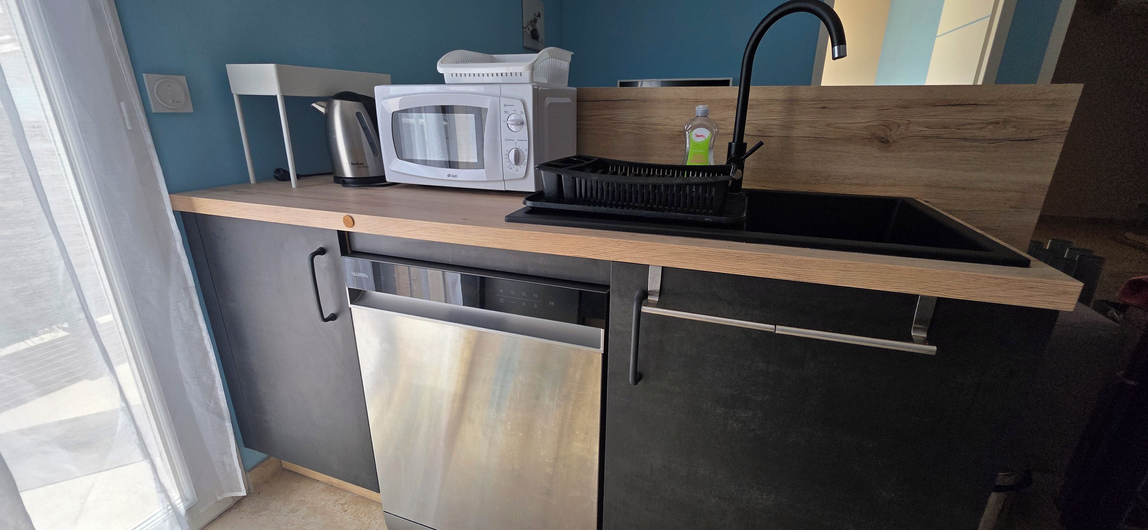 Une cuisine compacte équipée d’un four à micro-ondes, d’une bouilloire et d’un évier avec un robinet.