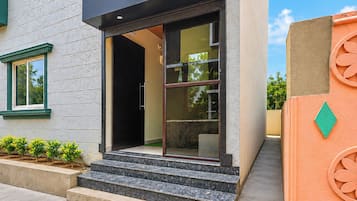 A modern building with a glass entrance, a set of steps leading up to it, and a small garden area with plants.