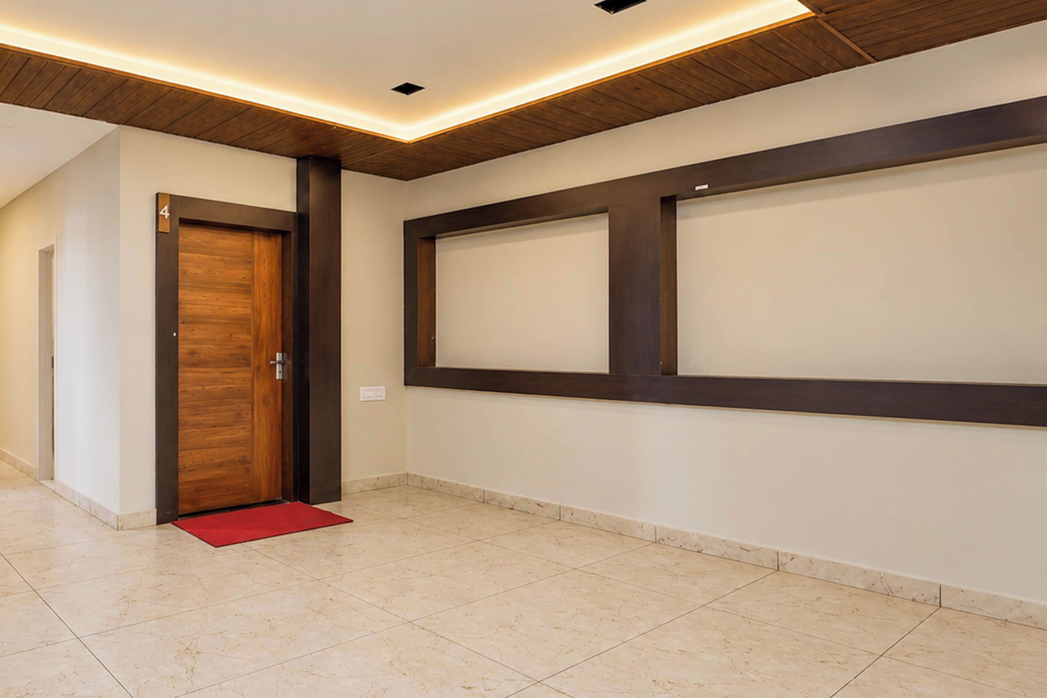 Un pasillo con una puerta de madera, un felpudo rojo y una pared con un panel oscuro grande.
