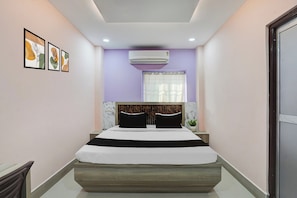 A bedroom with a bed, a window with a curtain, an air conditioning unit, and framed artwork on the wall. - Hotel O Maheshwari Heights (Cuttack)
