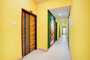 A hallway with yellow walls, a wooden door with a number sign, and a large mural on the right wall. - Hotel O Maheshwari Heights (Cuttack)
