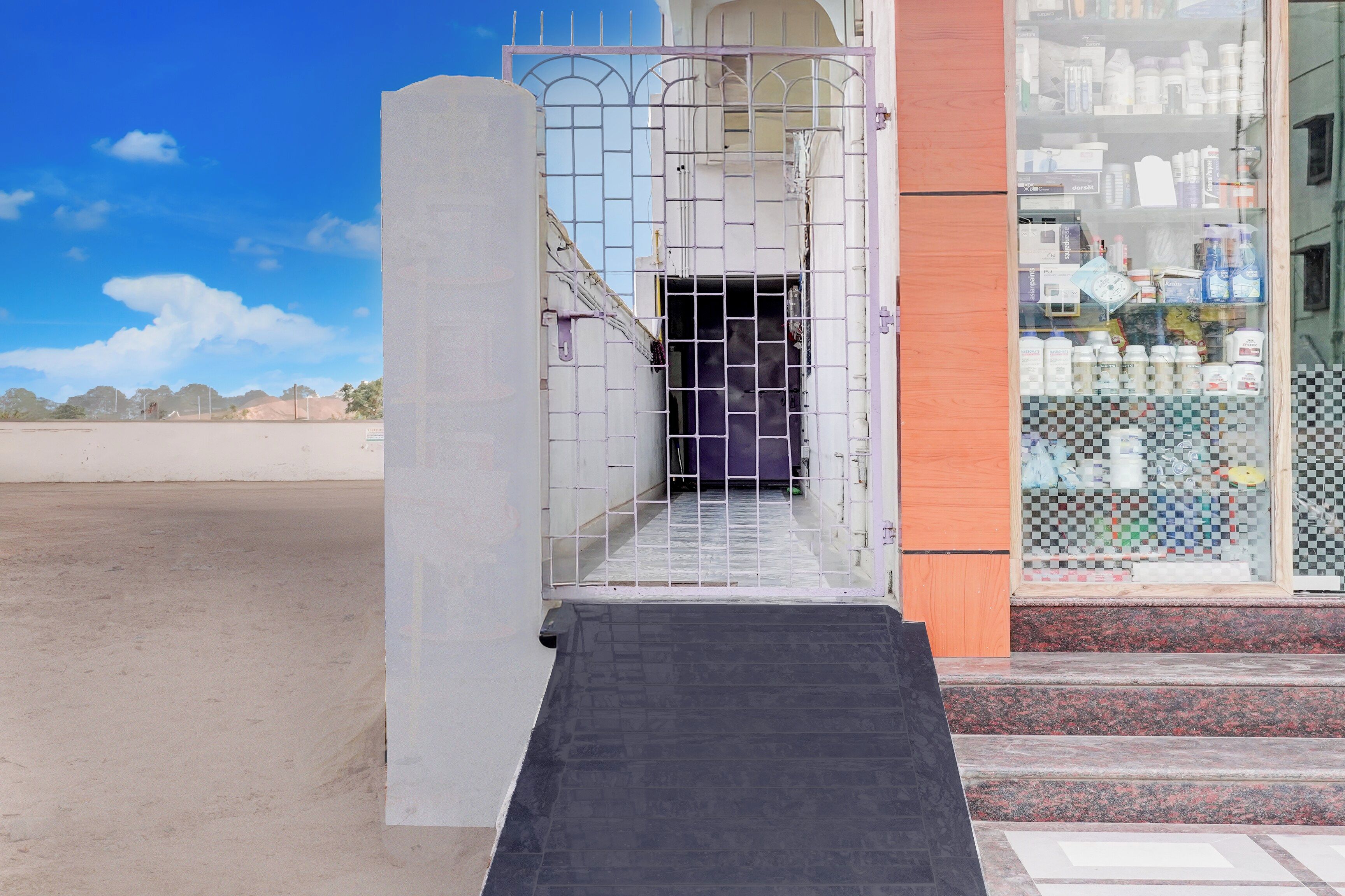 Entrada de edificio con puerta protegida por un portón, rampa de acceso y una tienda con diversos productos a la vista.