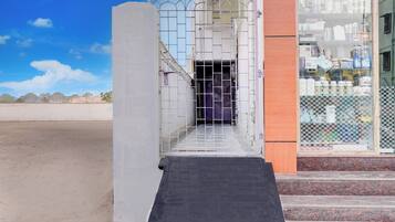 Entrada de edificio con puerta protegida por un portón, rampa de acceso y una tienda con diversos productos a la vista.