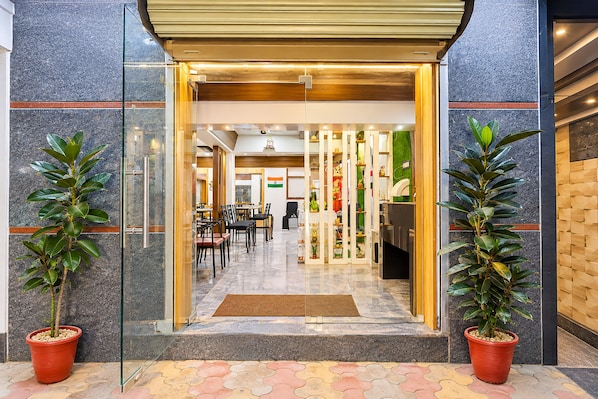 A hotel entrance with a glass door, potted plants, and a tiled floor.