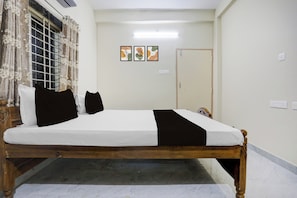 A bedroom with a bed, curtains, a door, and wall-mounted artwork. - Super Hotel O Kunjaban residency Barang (Cuttack)