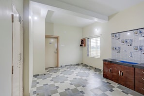 A room with a tiled floor, a window with bars, a wall-mounted shelf with kitchen items, and a door with a number. - Super Hotel O Kunjaban residency Barang (Cuttack)