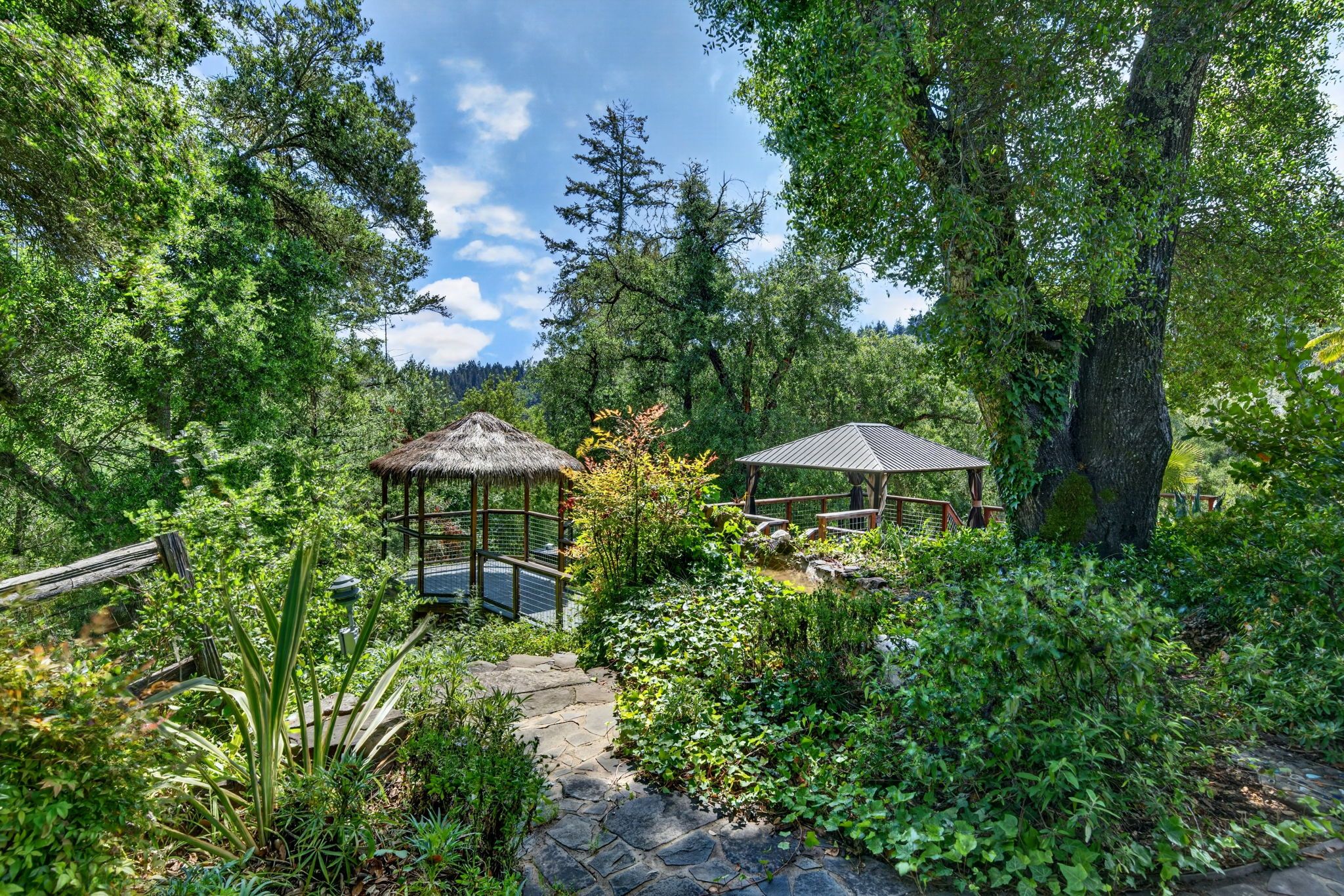 A garden with two gazebos, a stone pathway, and lush greenery.
