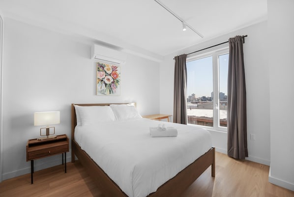 Une chambre d’hôtel avec un grand lit, une table de chevet avec une lampe, un tableau au mur et une vue sur la ville par la fenêtre.