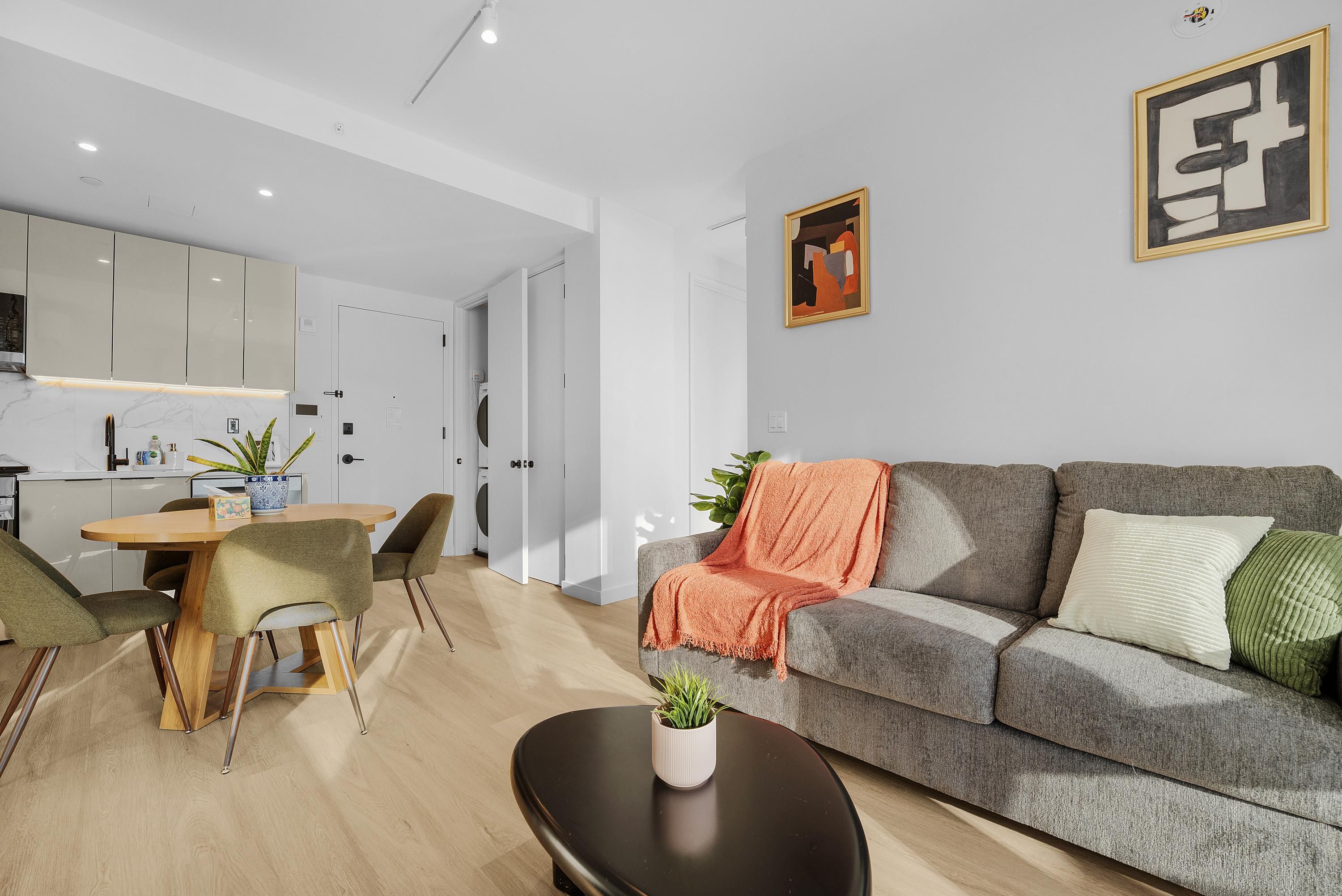 A modern living room with a grey sofa, a coffee table, and a dining area with a wooden table and chairs.
