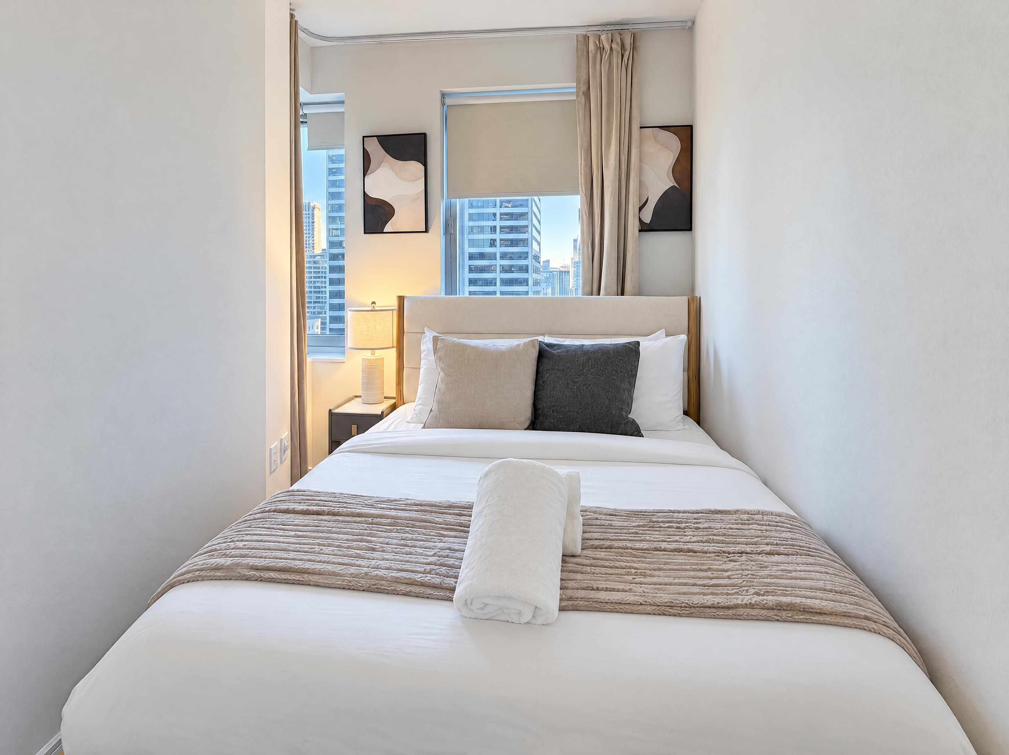 Ein Hotelzimmer mit einem Bett, einem Nachttisch, einer Lampe und einem Fenster mit Vorhängen.