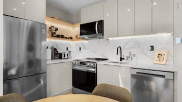 Una cocina moderna con electrodomésticos de acero inoxidable, un salpicadero de mármol y un comedor con mesa y sillas de madera.