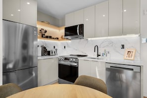 Une cuisine moderne dotée d’appareils électroménagers en acier inoxydable, d’un pare-feu en marbre et d’un coin repas avec une table et des chaises en bois.