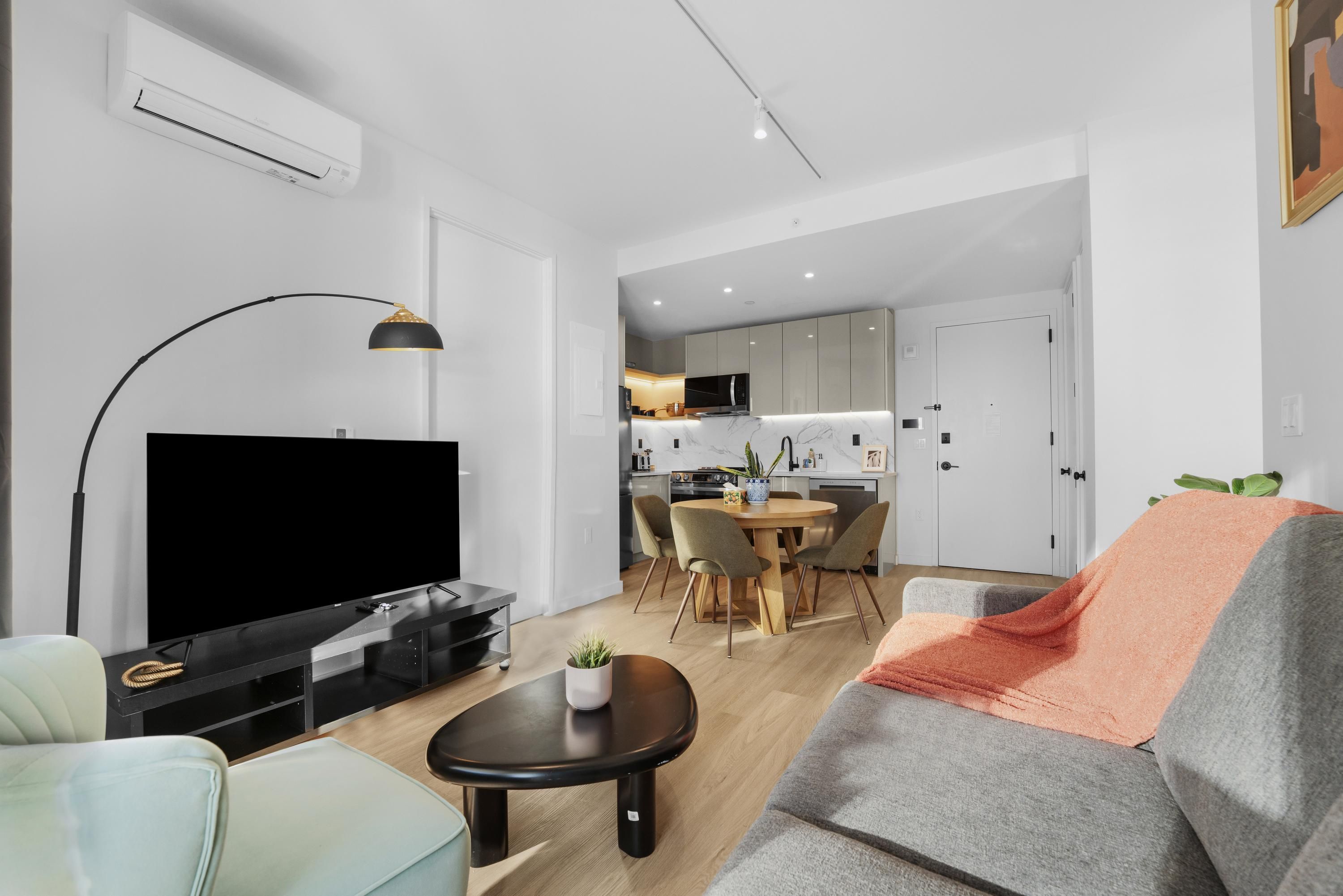 A modern living room with a flat-screen TV, a sofa, a coffee table, and a dining area with a table and chairs.