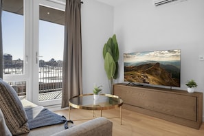 Un salon moderne doté d’un grand téléviseur à écran plat, d’une table basse en verre, d’un canapé et offrant une vue sur le paysage urbain grâce à une porte-fenêtre coulissante.