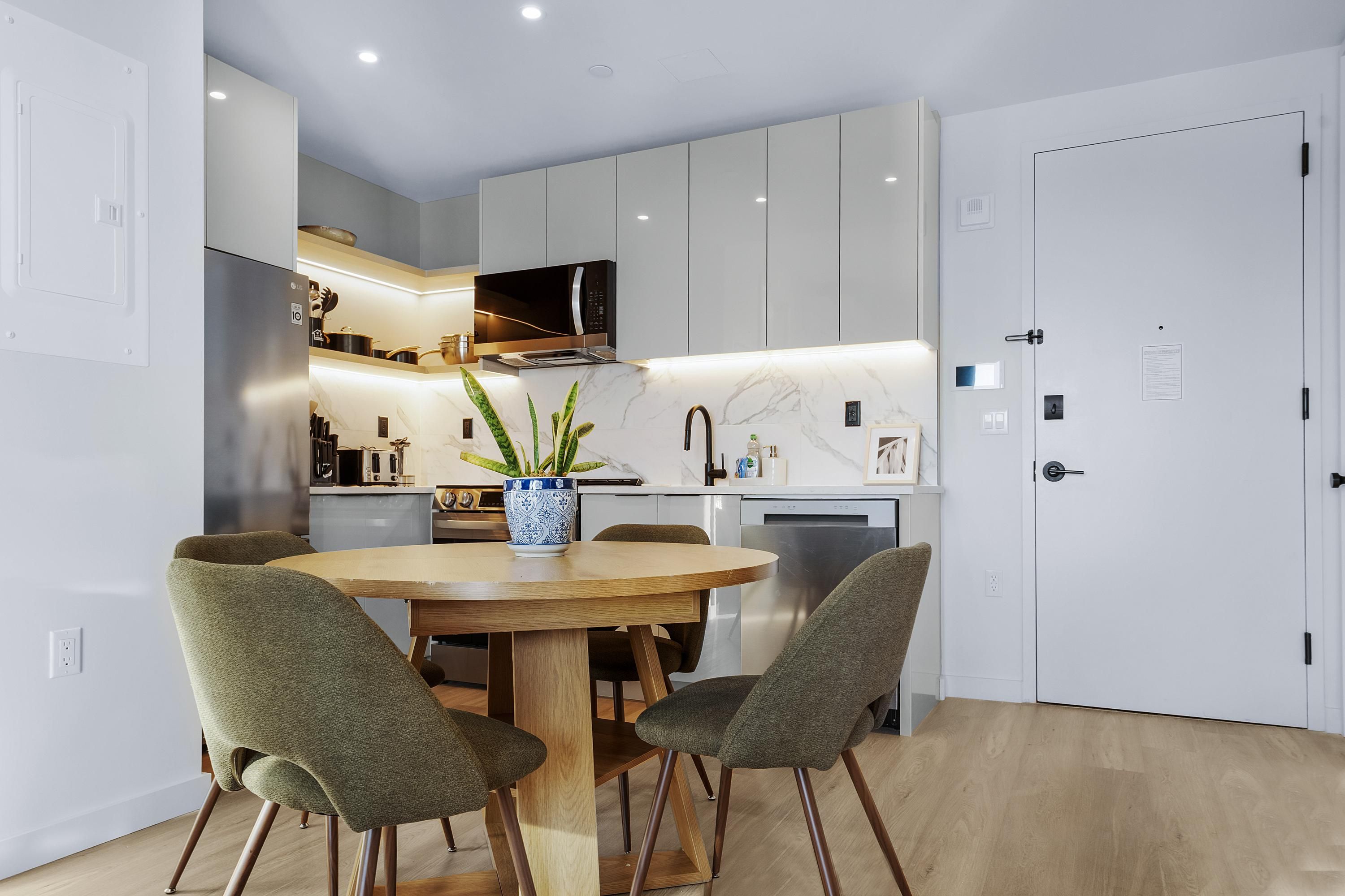A modern kitchen with white cabinets, a wooden dining table, and four green chairs.