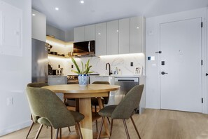 A modern kitchen with white cabinets, a wooden dining table, and four green chairs.