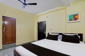 Ein Hotelzimmer mit Bett, Deckenventilator, Tür und Lichtschalter an der Wand.