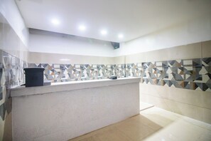 A bathroom with a tiled wall, a sink, and a trash bin. - Hotel O by OYO Prabir Residency Inn (Cuttack)