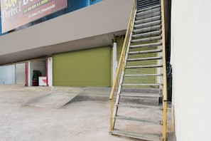 A building with a closed green shutter, a metal staircase leading to a landing, and a sign above advertising a room. - Hotel O by OYO Sun Perfect Lodge (Cuttack)