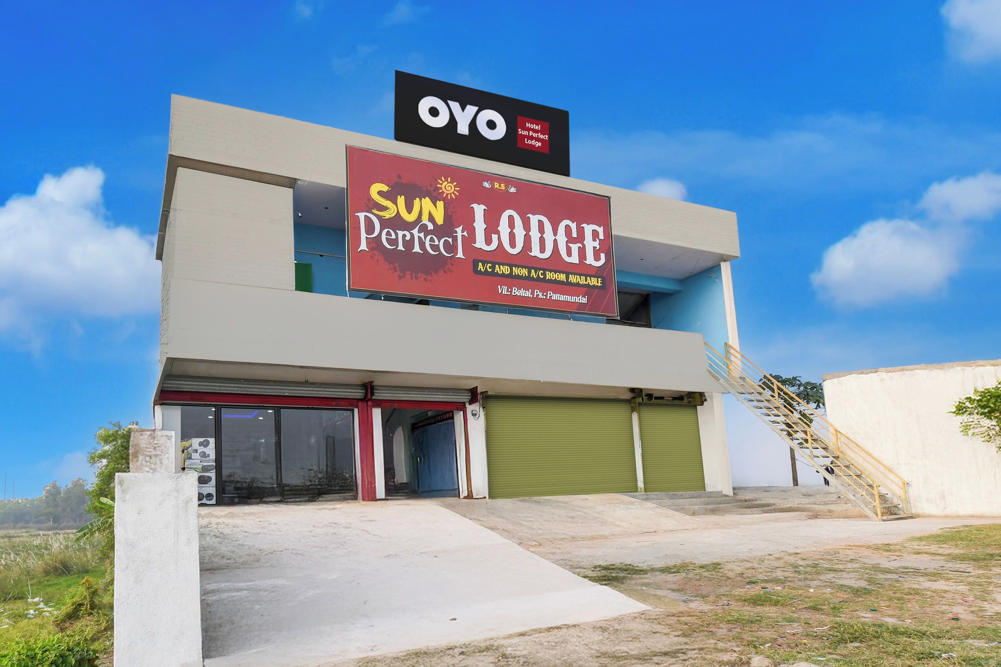 Een gebouw met twee verdiepingen, met een bord waarop 'OYO Hotel Sun Perfect Lodge' staat en een bord dat 'Kamers met en zonder airconditioning beschikbaar' aangeeft.