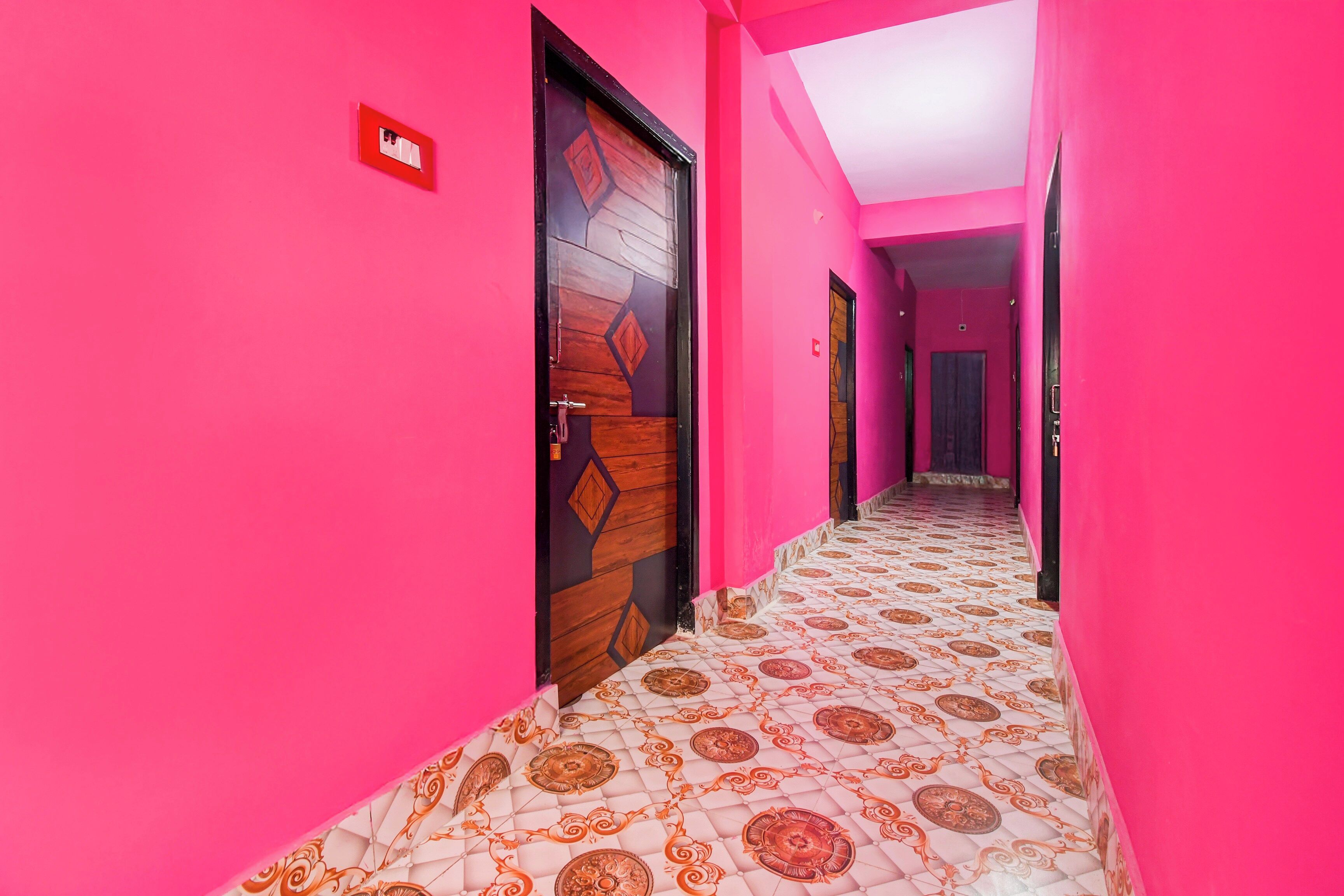 Een hal met roze wanden en een vloer met een patroon, die leidt naar een deur met een geometrisch ontwerp.