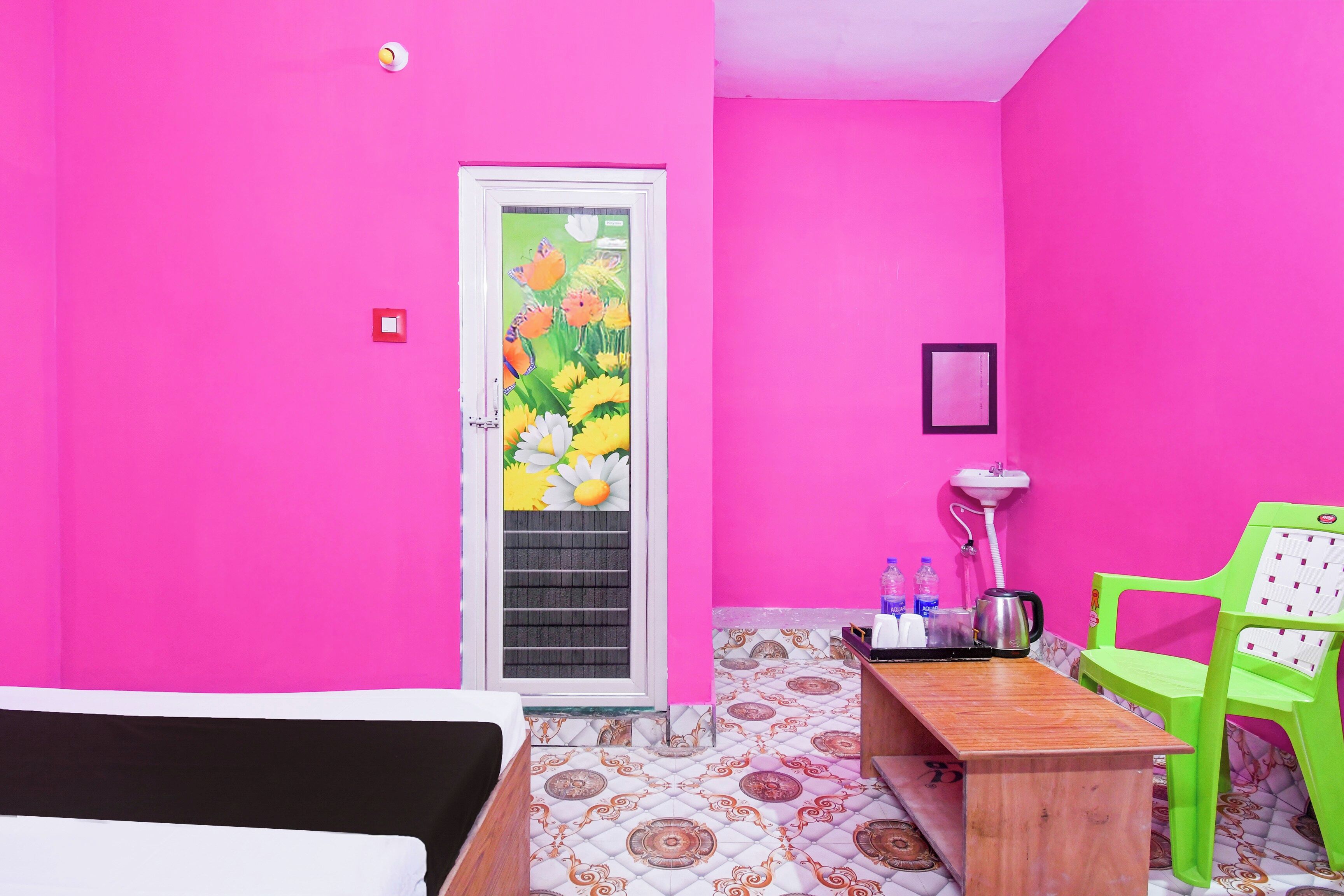 Una habitación con una cama, una mesa de madera, una silla verde, un lavabo y una puerta con un diseño floral colorido.