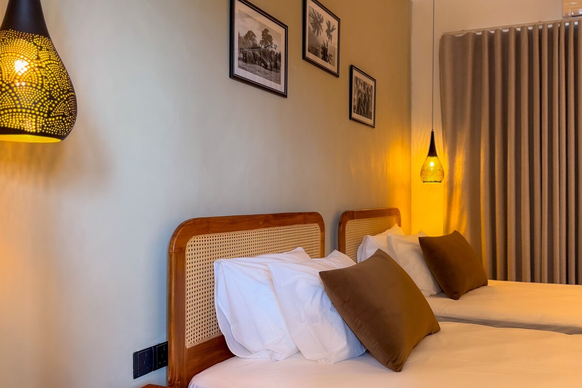 Une chambre d’hôtel avec deux lits, une grande fenêtre avec des rideaux et des cadres photo accrochés au mur.