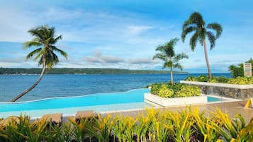 Piscina com vista para o oceano, cercada por palmeiras e plantas tropicais.