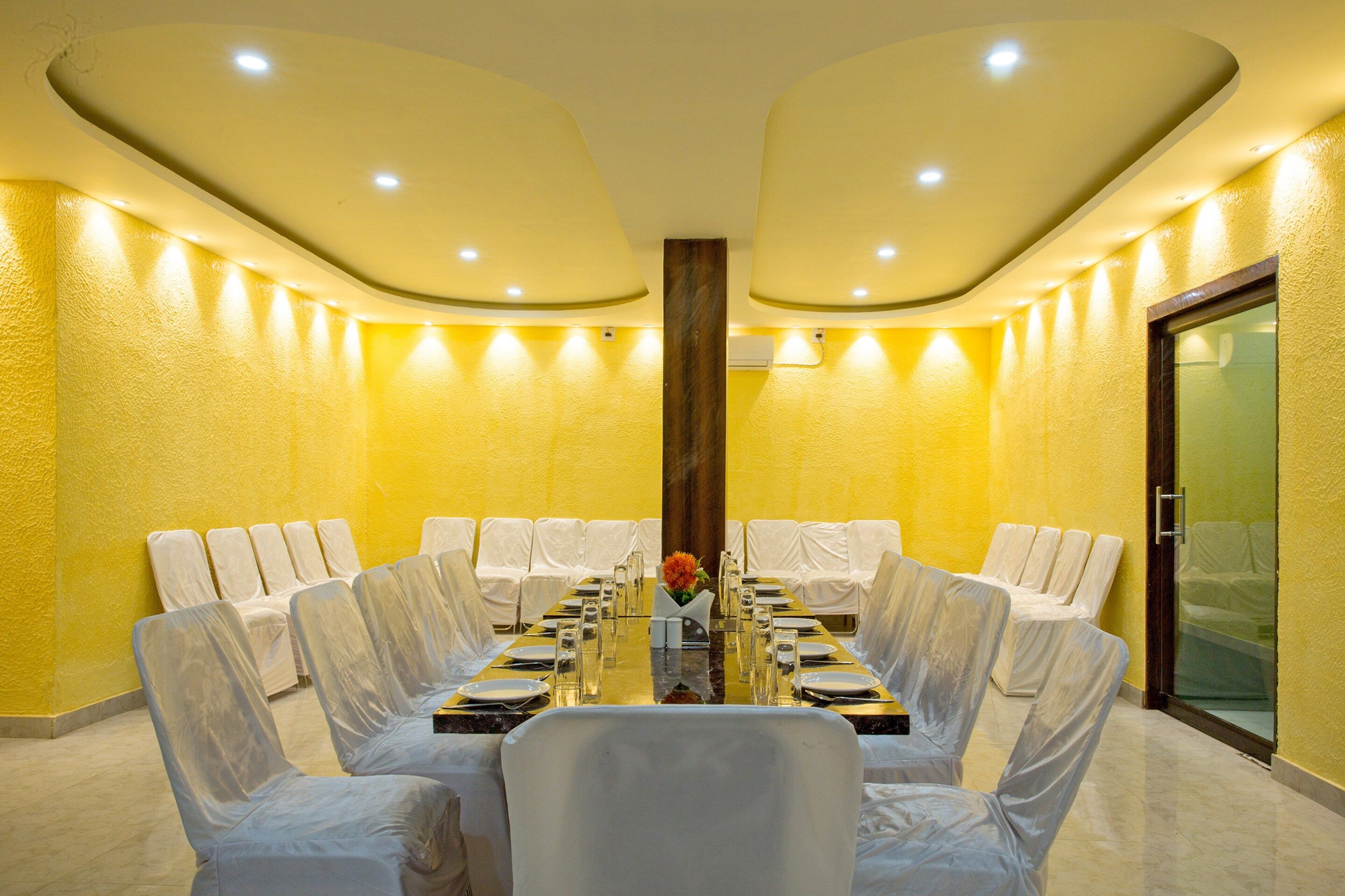 Un salón de conferencias con una mesa redonda, sillas blancas y una pared de vidrio.
