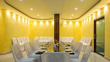 Un salón de conferencias con una mesa redonda, sillas blancas y una pared de vidrio.