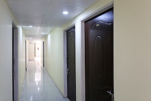 A corridor with two dark wooden doors, a tiled floor, and a ceiling with recessed lighting.