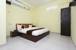 A hotel room with a bed, a nightstand, an air conditioning unit, a wardrobe, and a flat-screen TV.