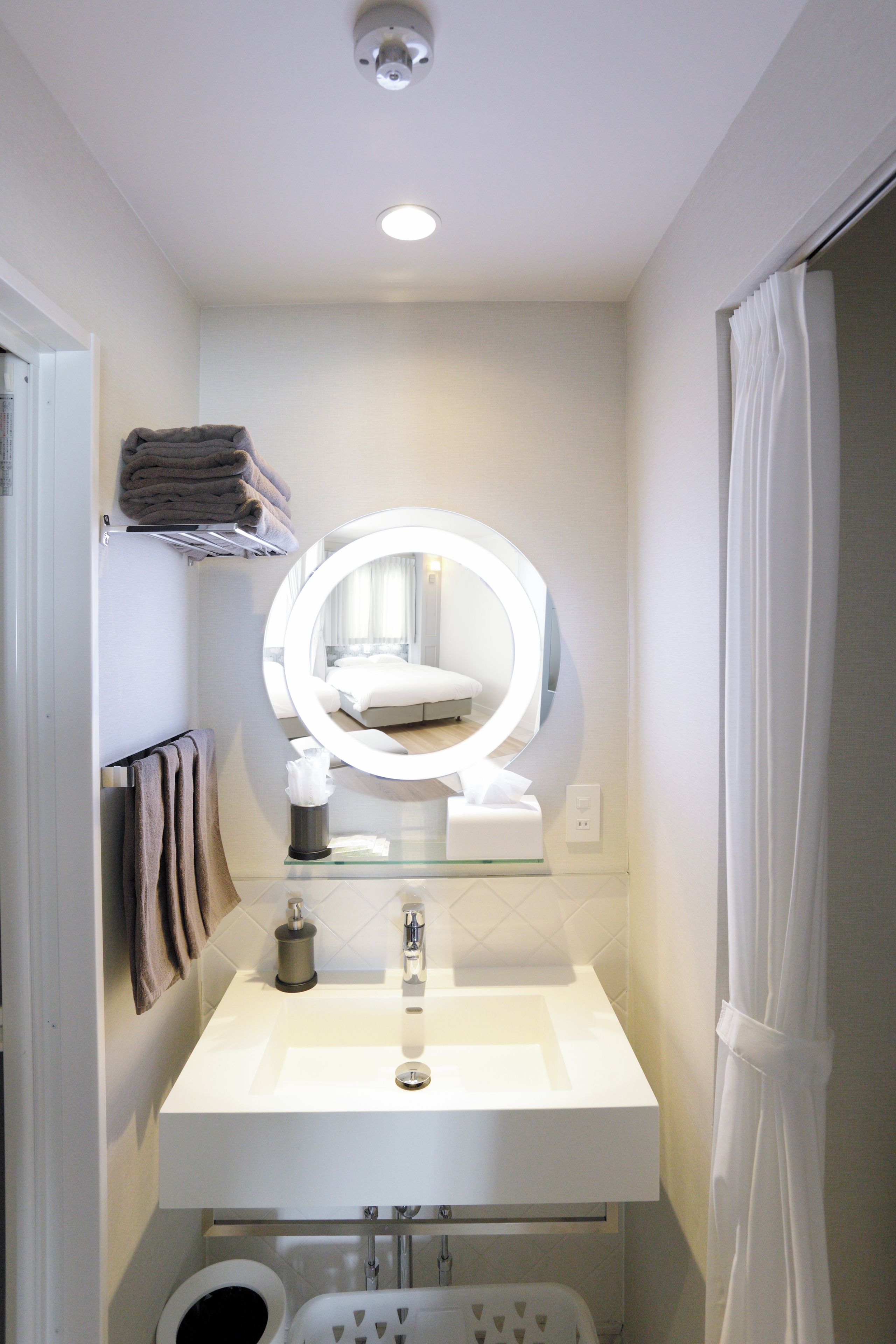 Un baño con un lavamanos blanco, un espejo con luces, un perchero y una cortina de ducha.
