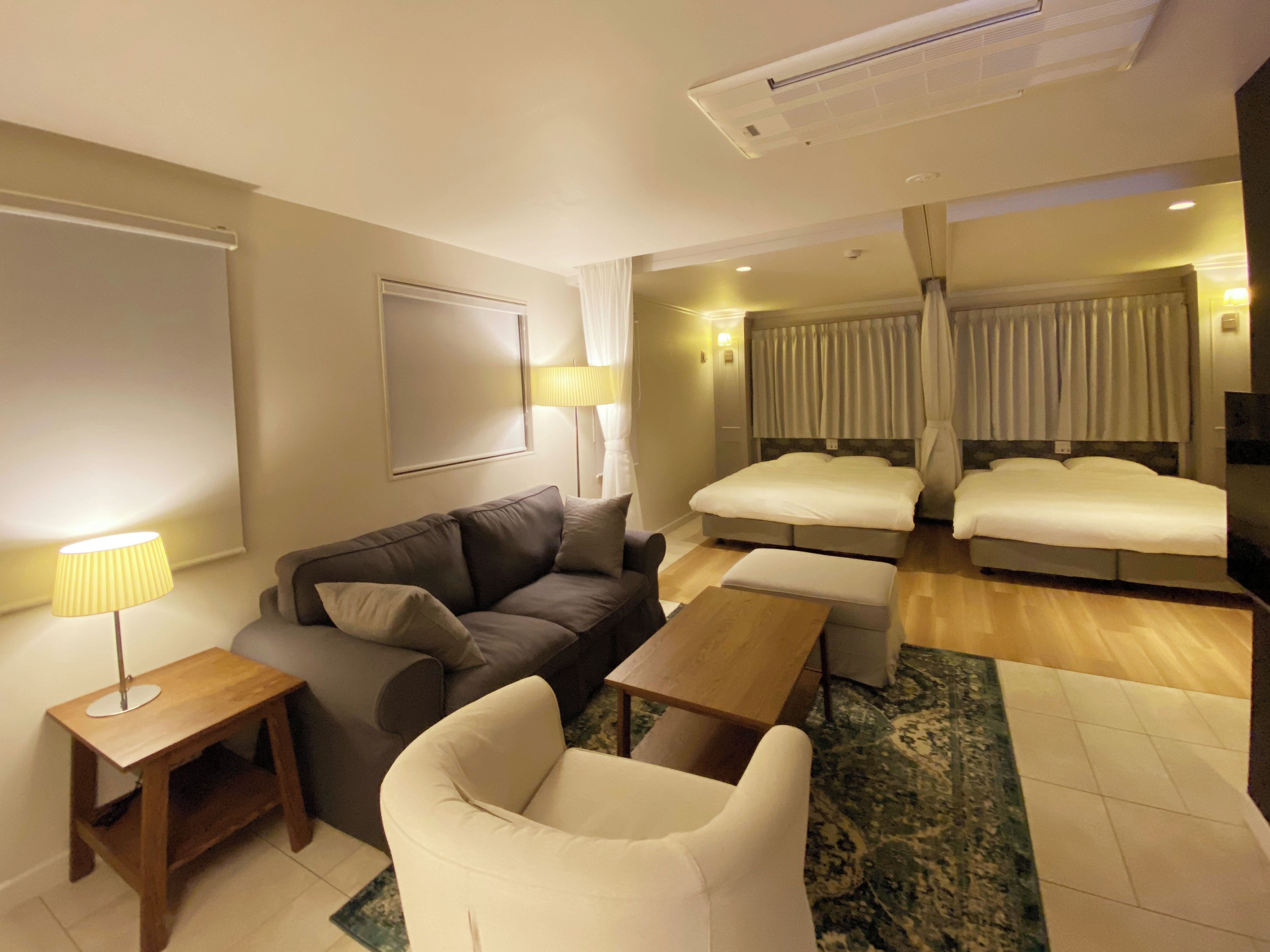 Habitación de hotel con sofá, una silla, una mesita, cama con cortinas, televisor y lámpara.