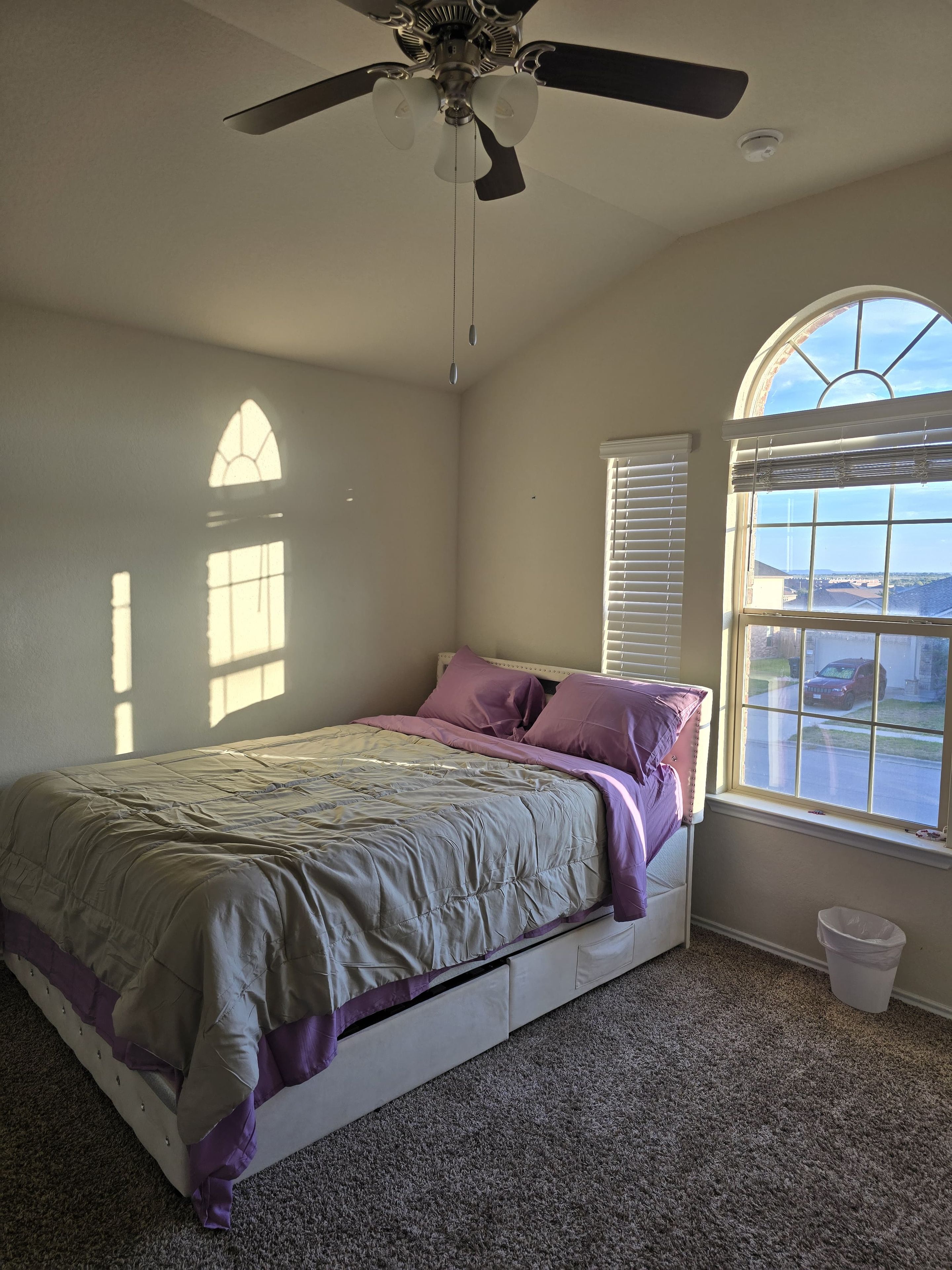 Une chambre à coucher avec un lit, un ventilateur de plafond, une fenêtre avec des stores et une vue sur l’extérieur.