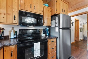Une cuisine avec des meubles de rangement en bois, un micro-ondes noir, un réfrigérateur en acier inoxydable et un four noir.