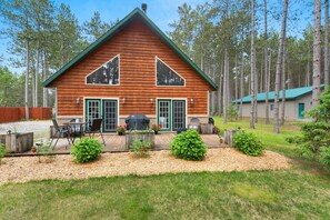 Une cabane avec un toit végétalisé, deux cheminées et une terrasse aménagée avec du mobilier d’extérieur.